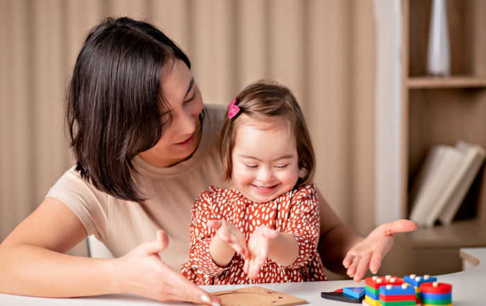 child with down syndrome with educational toys smiles, a cute girl with her special needs nanny